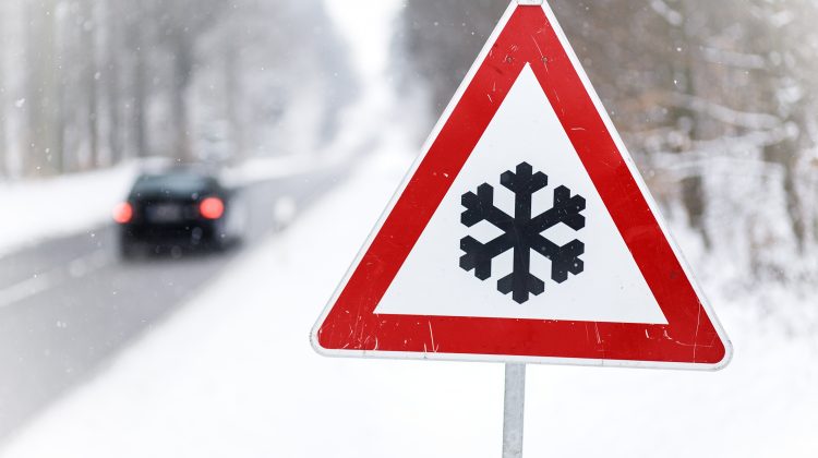 Traffic sign showing snow ahead, car driving on snow plowed road in background
