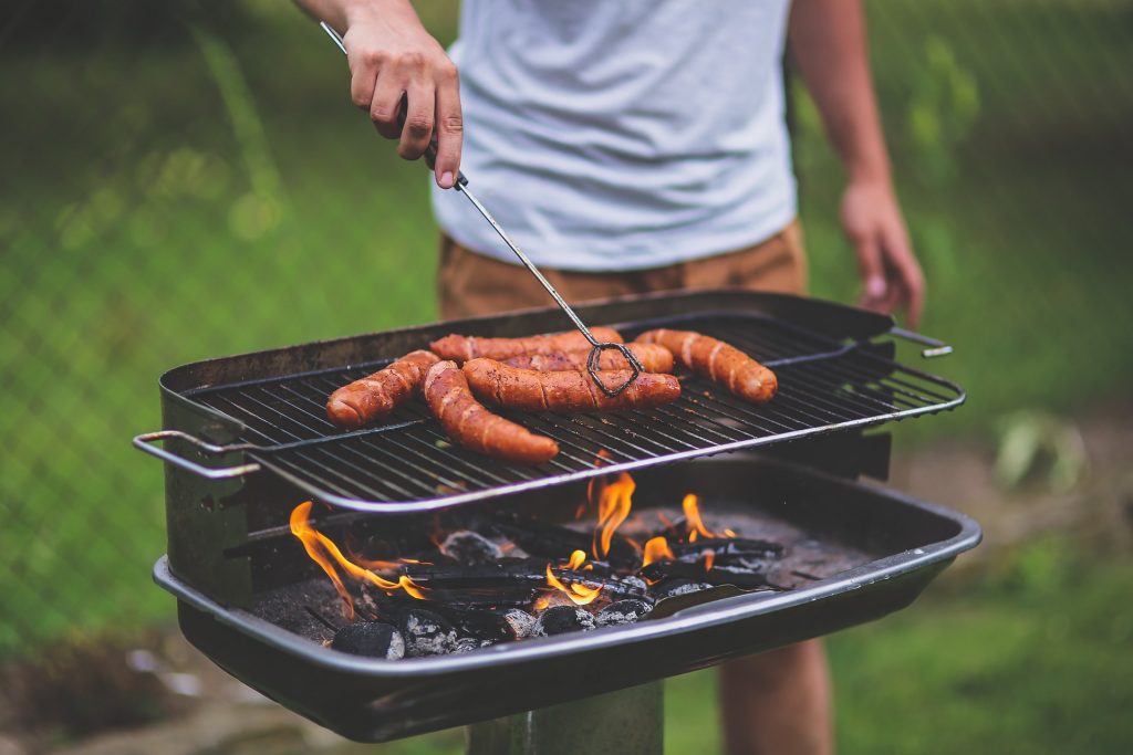 A man grilling large sausages on an outdoor grill