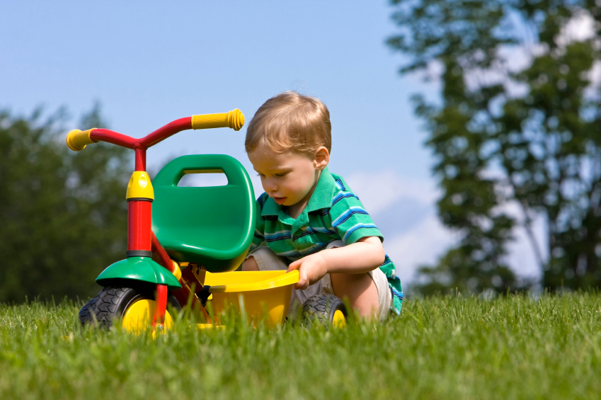 Boy in grass playing with tricycle