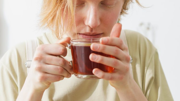 Thin person cups brings a cup of tea to their mouth