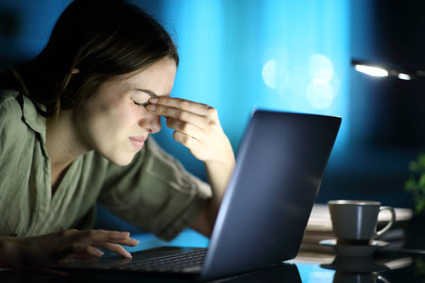 Woman pinching eyes closed due to eye strain from using laptop at night
