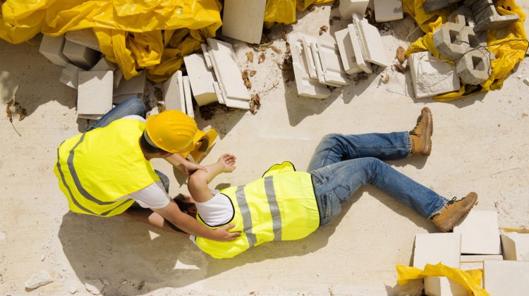 image of two construction workers, one of which is injured and lying on the ground of the construction site