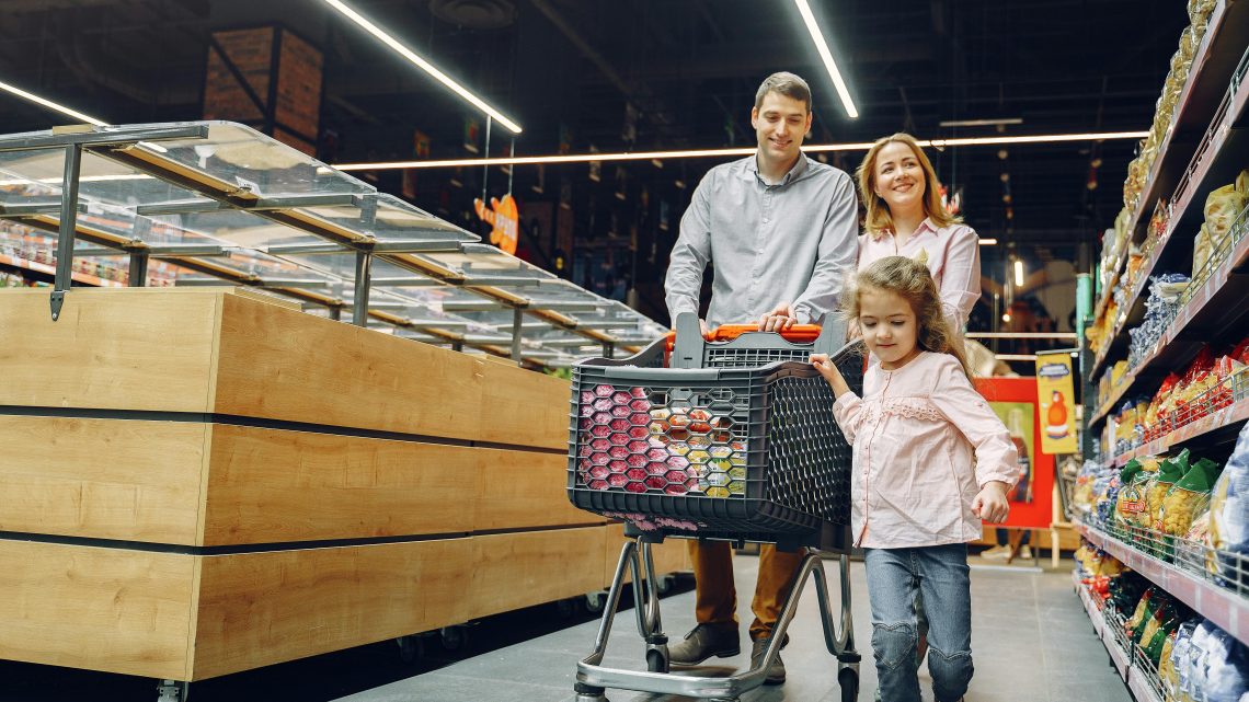 Family of three walking with shopping cart at a grocery store.