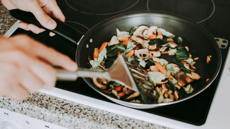 Someone cooking vegetables on a non-stick pan with a metal spatula