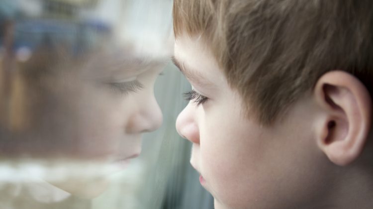 a sad child looking at a window with their reflection looking back